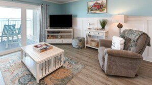 A living room with a television, a sofa, a coffee table, and a view to the outside. - Oceanfront 1 BR Condo with a Shared Pool! South Shores II 201 (Surfside Beach)