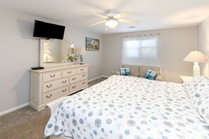Cozy retreat with a large bed, dresser, TV, and ceiling fan.