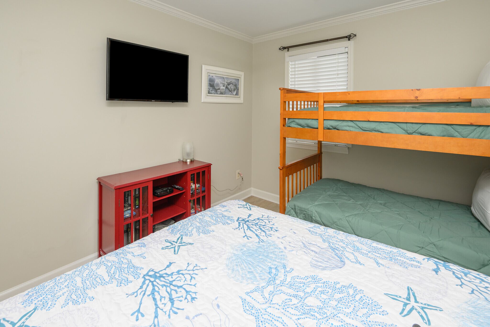 A bedroom with a bunk bed, a television mounted on the wall, a small red cabinet, and a framed picture.