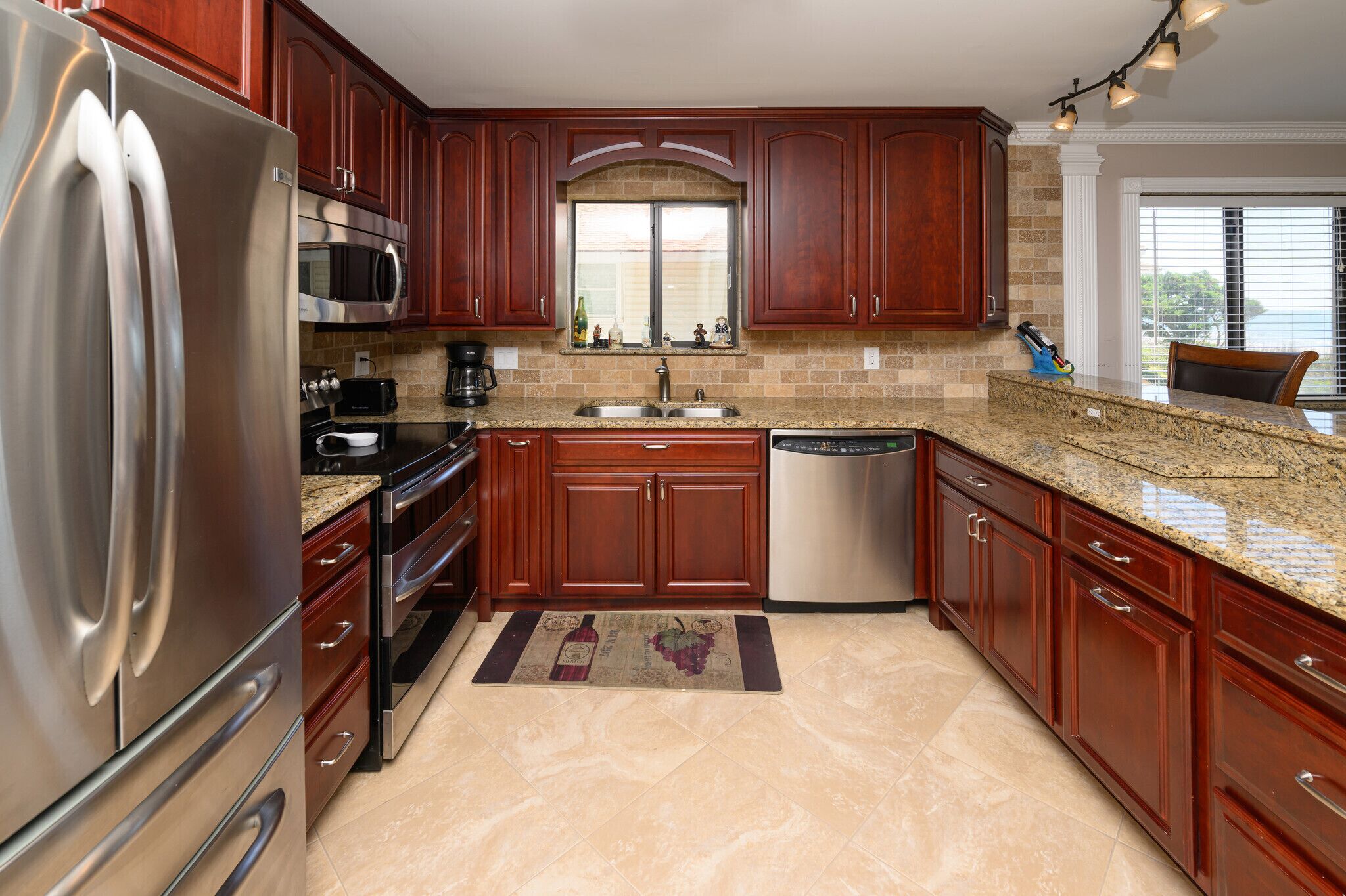 A kitchen with wooden cabinets, stainless steel appliances, a granite countertop, and a window with a view.