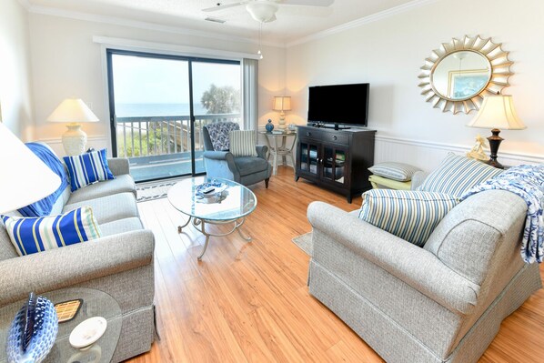 A spacious living room with a balcony, a flat-screen TV, and a decorative mirror.
