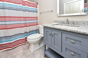 Bathroom features a striped shower curtain, a toilet, a granite countertop, and a light gray vanity with drawers and a cabinet.