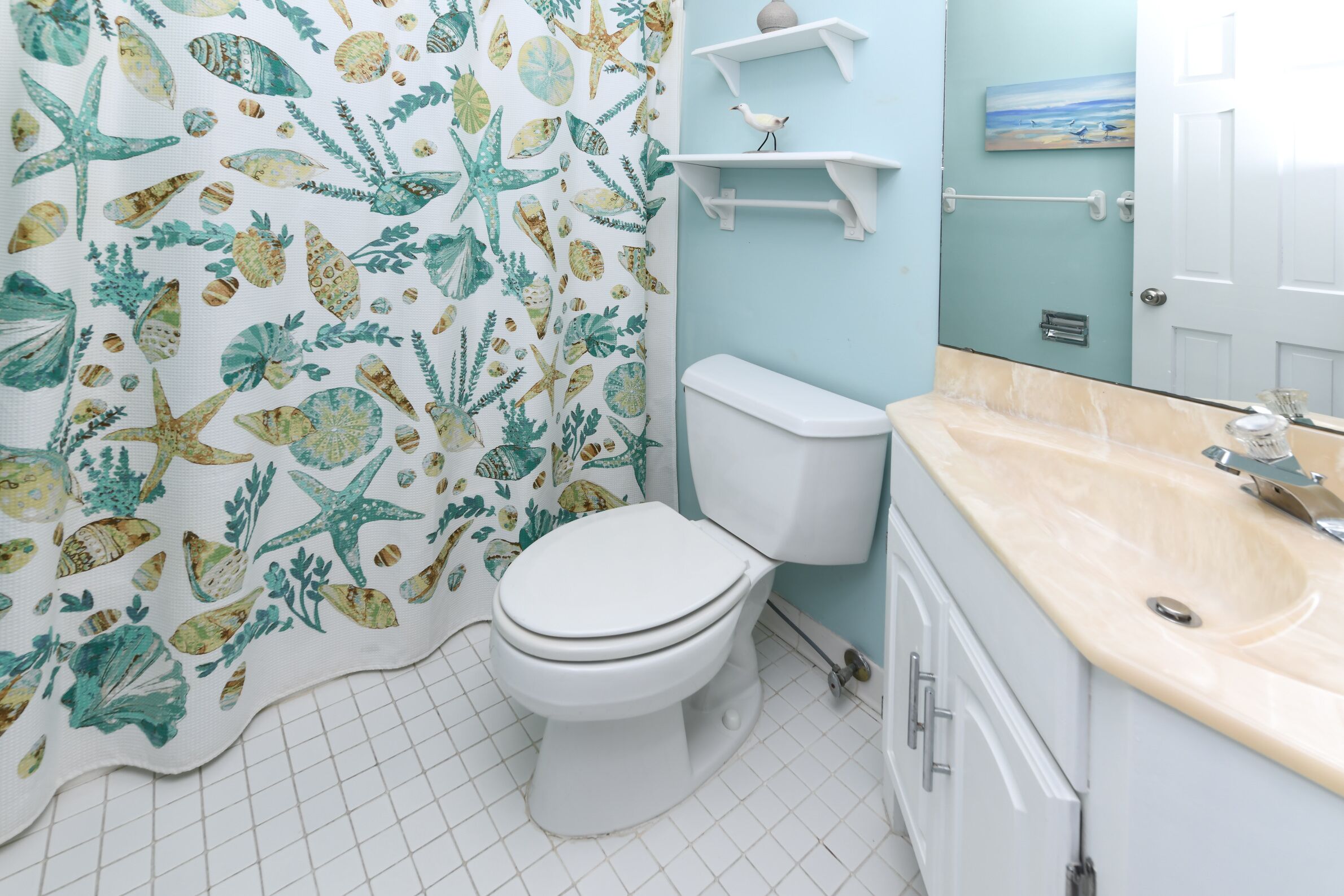 A bathroom with a white toilet, a beige countertop, and a shower curtain with a sea-themed pattern.