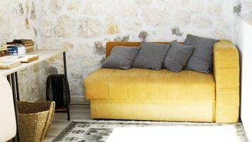 A cozy room with a yellow sofa, a stone wall, a small table with books, and a patterned rug.