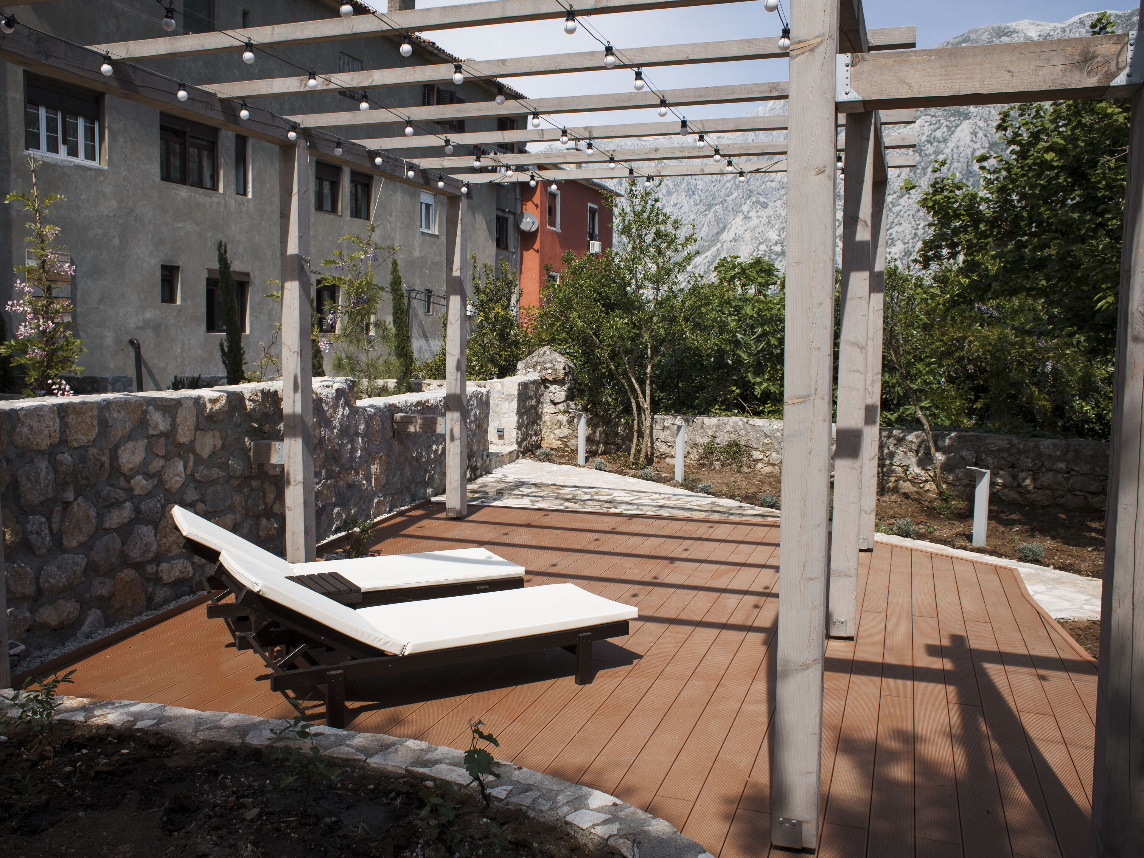 Una terraza de madera con dos sillones, un muro de piedra y un edificio con múltiples ventanas al fondo.