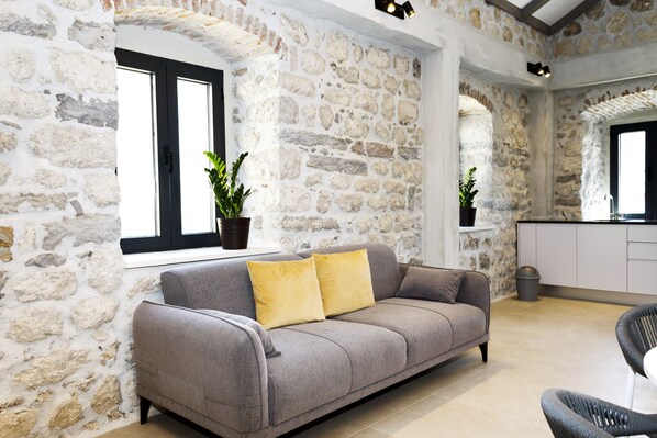 A stone-walled room with a grey sofa, two yellow cushions, and potted plants. - Galathea House (Kotor)