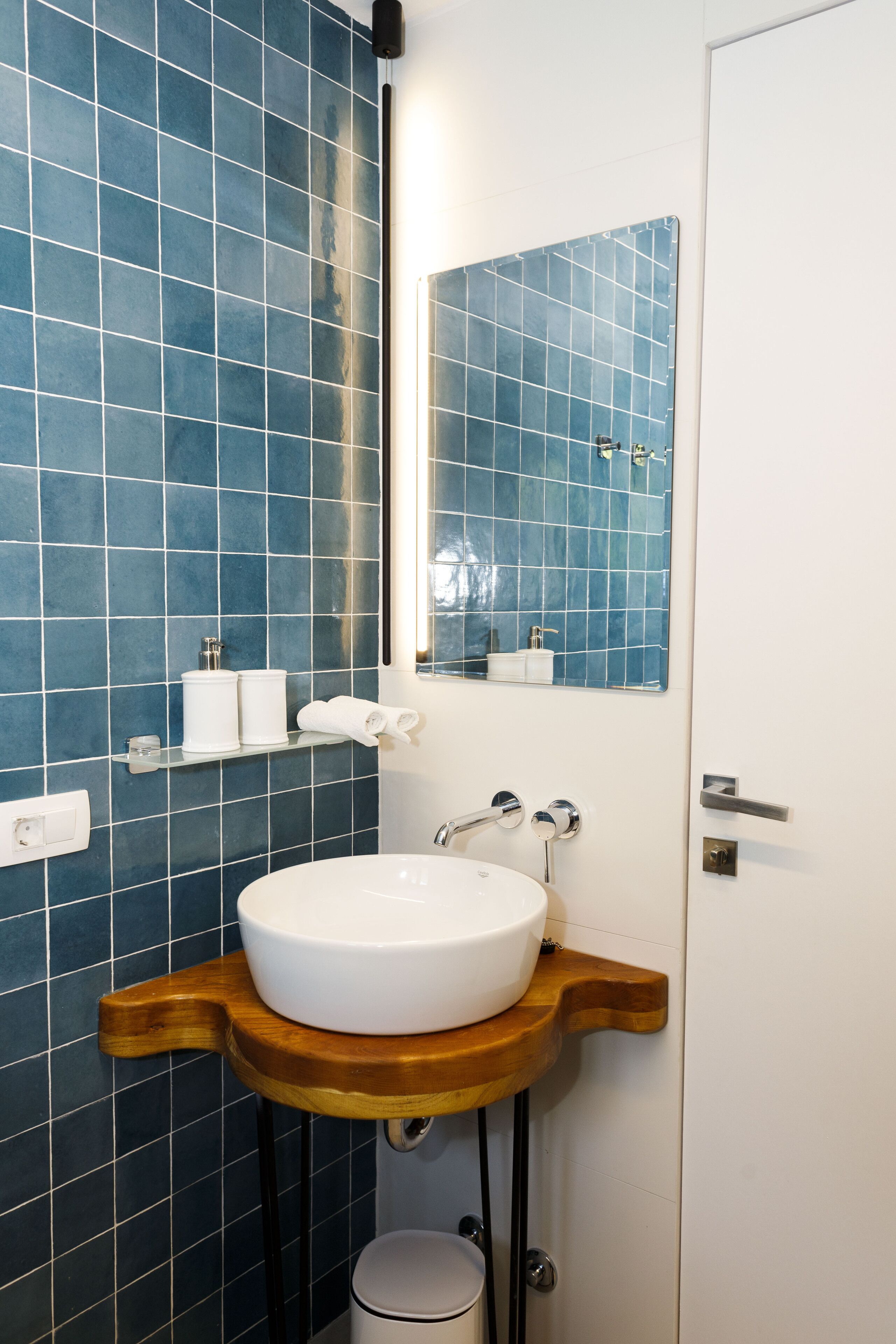 A bathroom with a white sink, blue tiled walls, a wooden countertop, and a mirror.