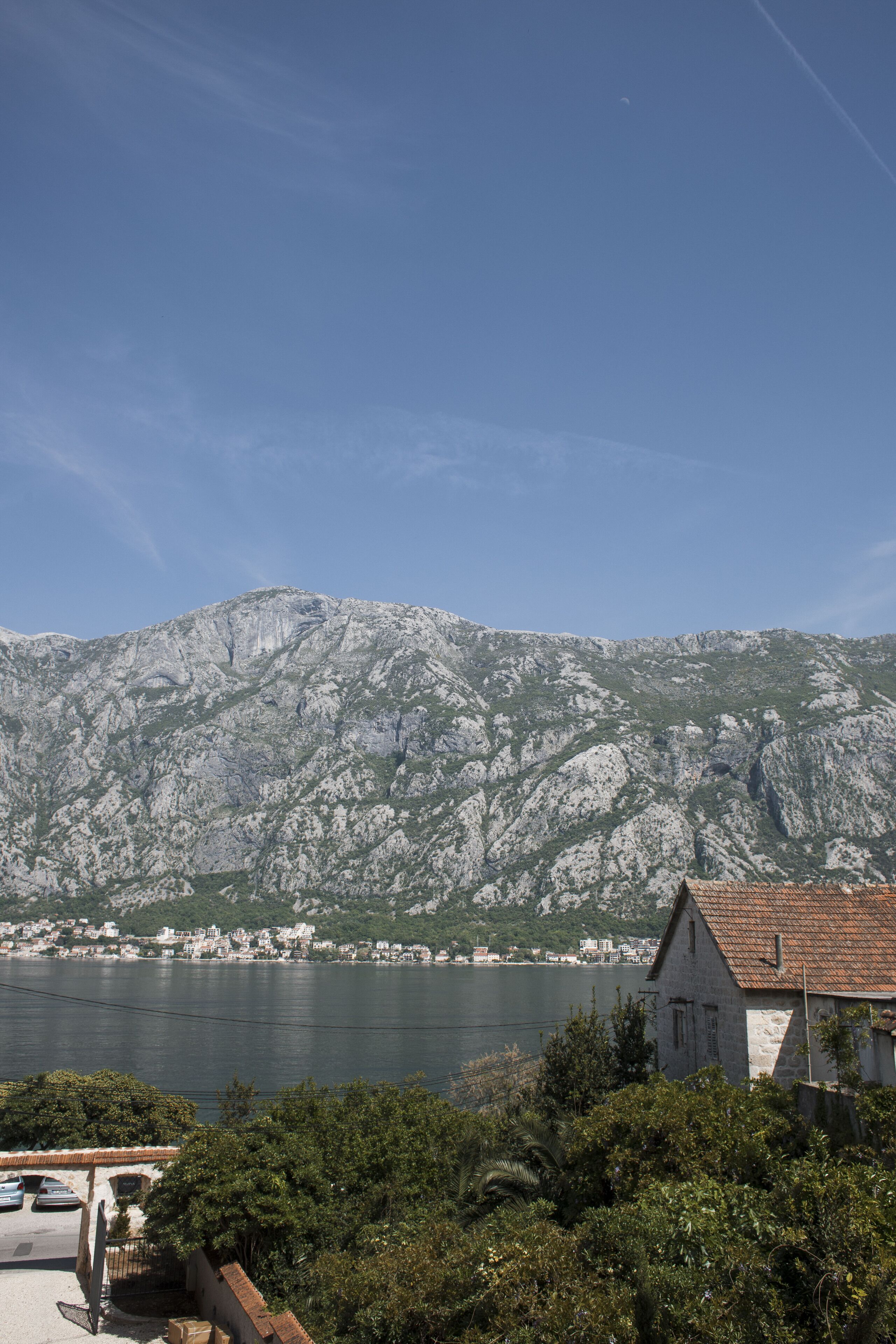 A coastal town with a mountain backdrop, a body of water, and a stone building with a tiled roof.