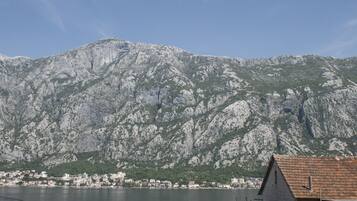 A coastal town with a mountain backdrop, a body of water, and a stone building with a tiled roof.