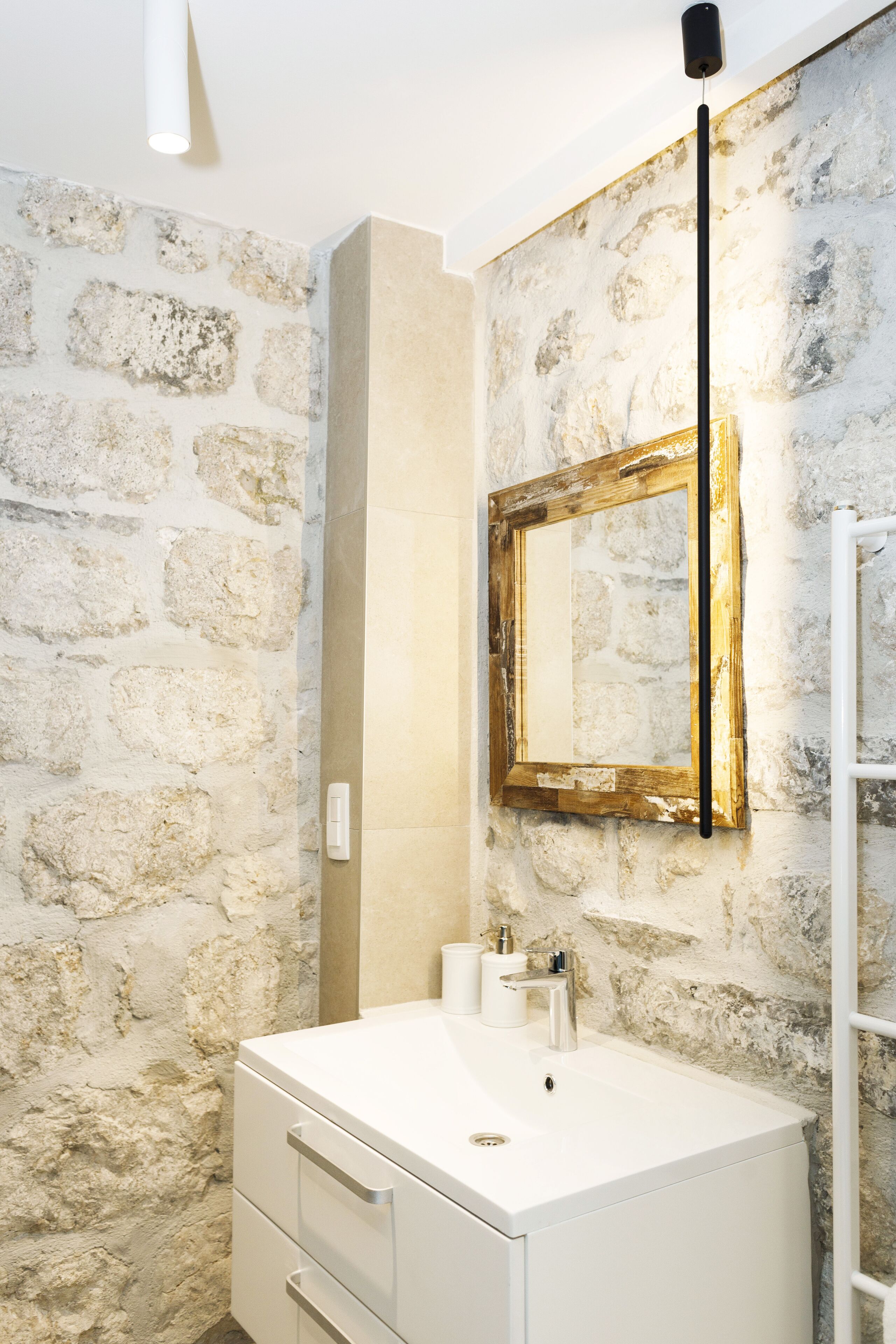 Un baño con pared de piedra, un lavamanos blanco, un espejo y un perchero para toallas.