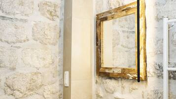 Un baño con pared de piedra, un lavamanos blanco, un espejo y un perchero para toallas.
