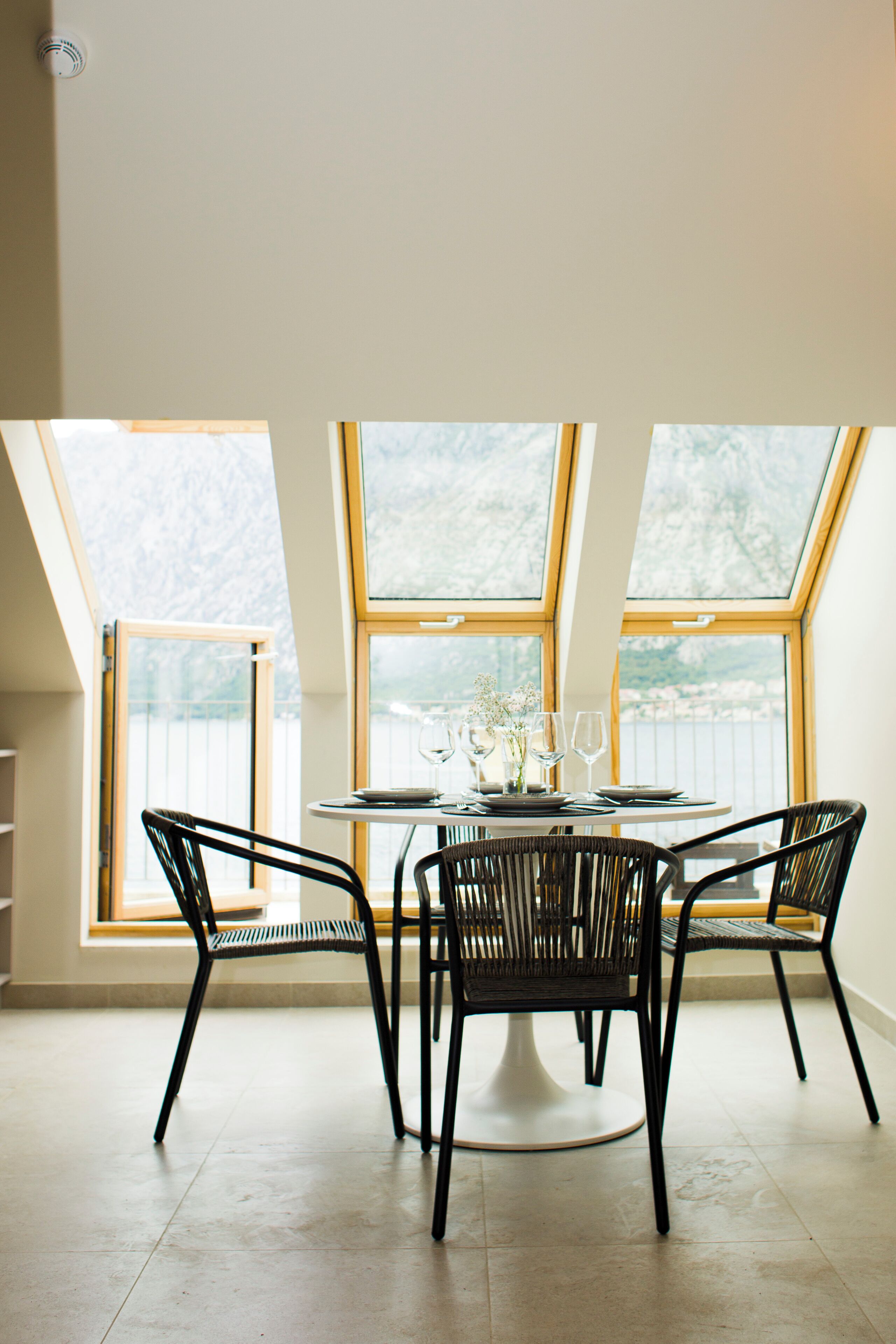 A dining area with a round table, four chairs, and a view through large windows.