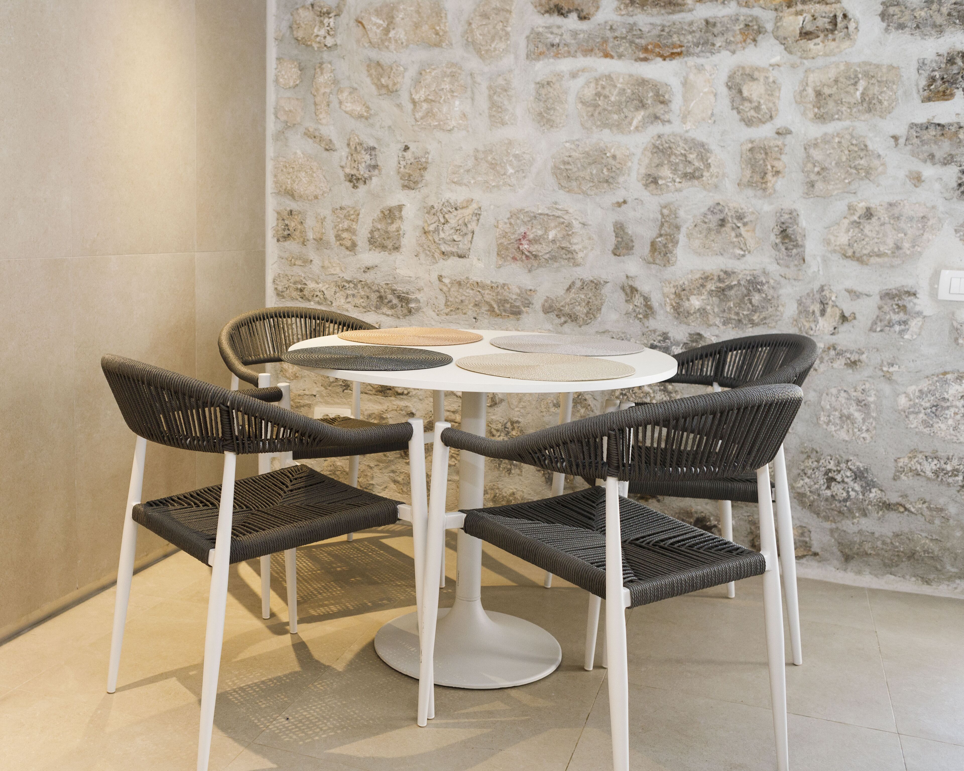 A round table with a white base surrounded by six wicker chairs with white legs.
