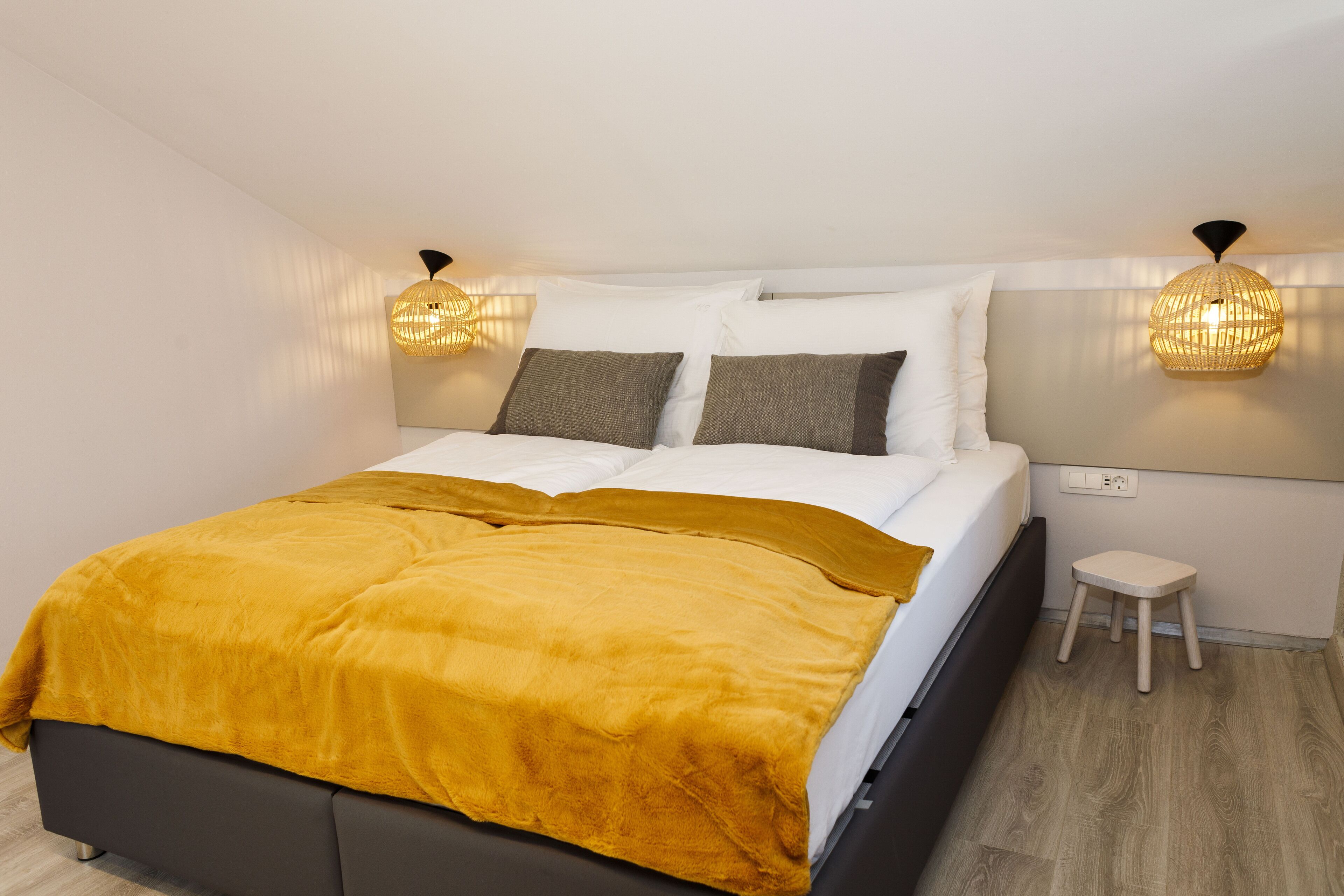 A modern bedroom with a bed, a bedside table, a small stool, and two wall-mounted lamps.
