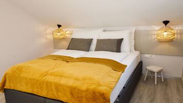 A modern bedroom with a bed, a bedside table, a small stool, and two wall-mounted lamps.