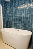 Un baño con bañera independiente, paredes de azulejos y una puerta a la vista.