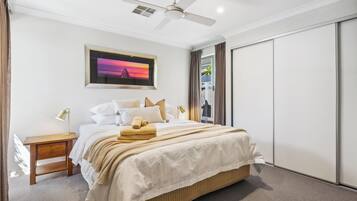 A bedroom with a bed, bedside tables, a ceiling fan, a framed picture, and a sliding door.