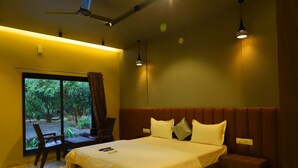 Una habitación de hotel con una cama grande, una zona de estar, un ventanal con vistas a zonas verdes y un ventilador de techo.