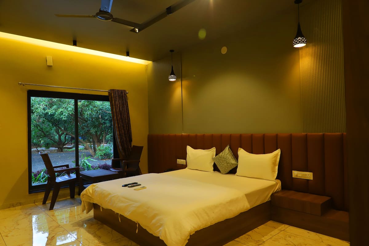 A hotel room with a large bed, a seating area, a window with a view of greenery, and a ceiling fan.