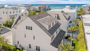 Un quartier résidentiel en bord de mer, avec des bâtiments blancs, une vue dégagée sur l’océan et une pelouse bien entretenue agrémentée d’une terrasse.