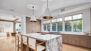 Une cuisine moderne avec un îlot en marbre, des chaises en bois et de grandes fenêtres.