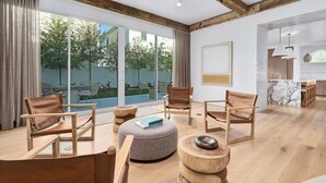 Un vaste espace de vie agrémenté de meubles en bois, de grandes fenêtres et d’une cuisine située au fond de la pièce.