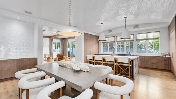 Une cuisine moderne dotée d’un grand îlot central, de tabourets de bar blancs et de luminaires suspendus.
