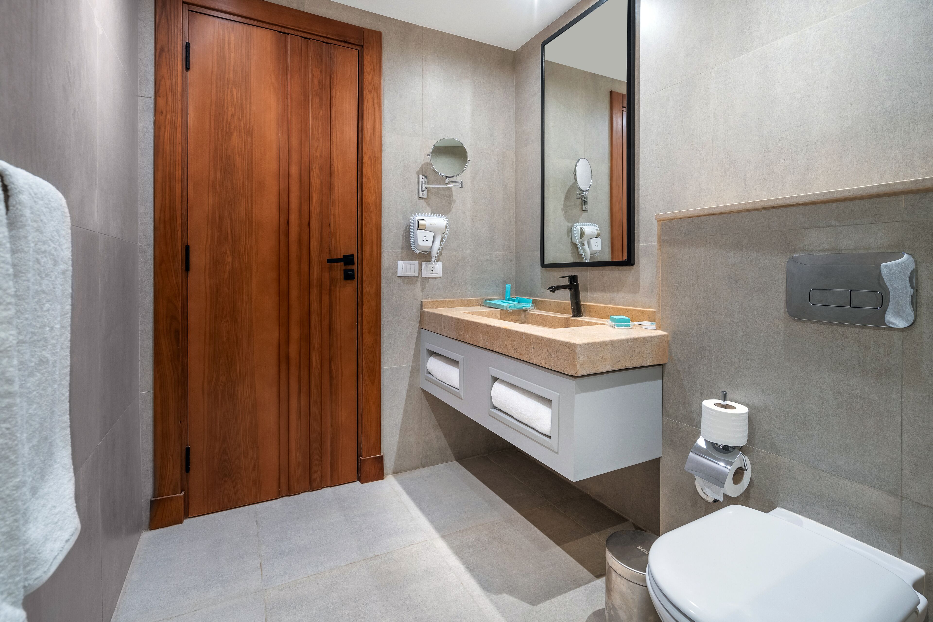 Ein modernes Badezimmer mit Holztür, Waschbecken mit Spiegel darüber, Toilette und Handtuchhalter.