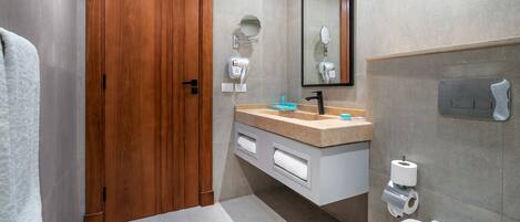 A modern bathroom with a wooden door, a sink with a mirror above, a toilet, and a towel rack.