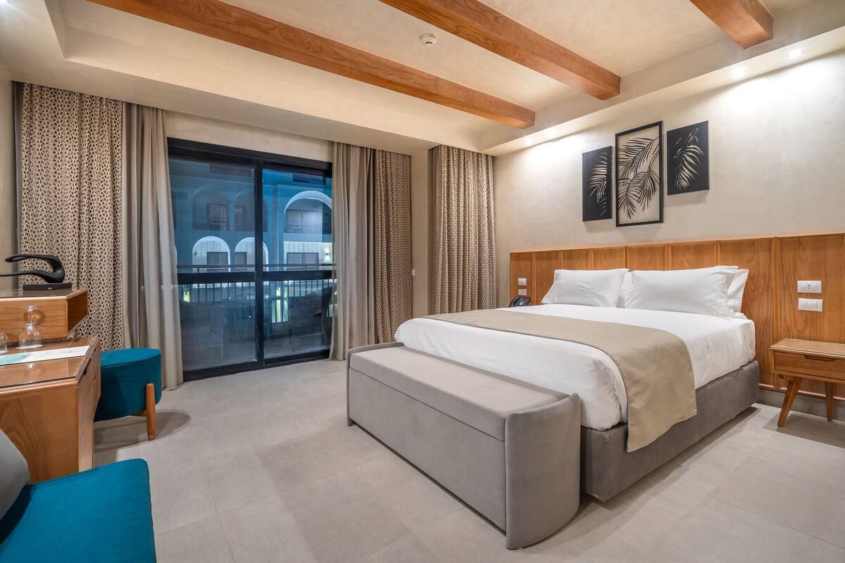 Une chambre d’hôtel moderne, dotée d’un grand lit, d’un bureau, d’une banquette et offrant une vue sur l’extérieur.