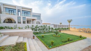 A modern building with a well-maintained garden, a paved pathway, and a beach view. - Al Masa Hotel El Sokhna (Ataqah)