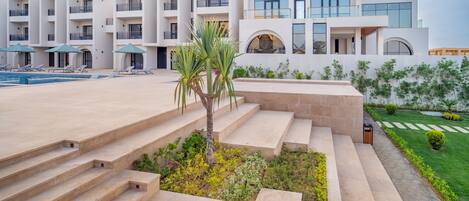 Un hotel moderno con varios balcones, piscina y un jardín bien cuidado.