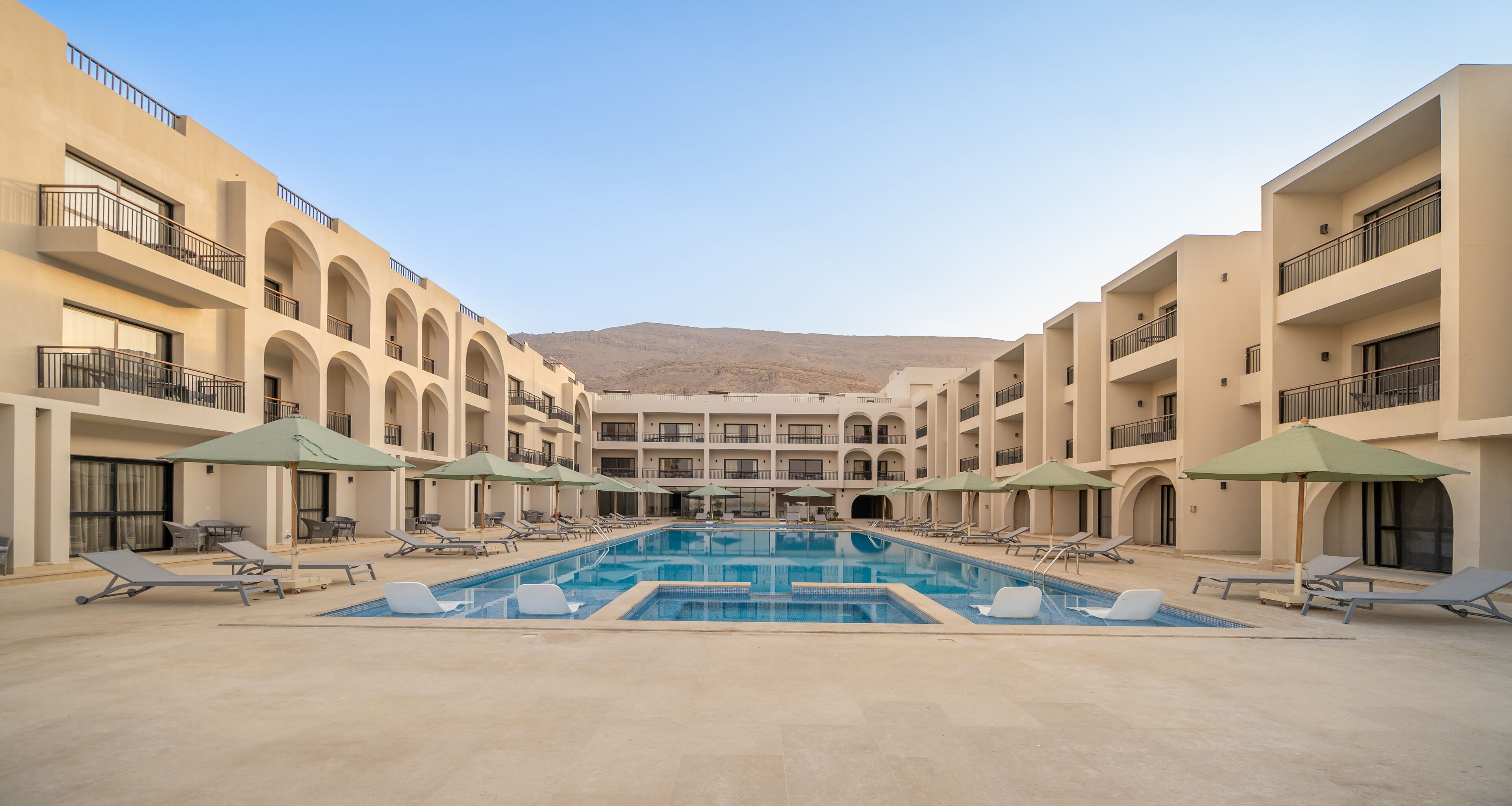 A hotel courtyard with a swimming pool, sun loungers, and umbrellas.