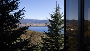 A view through a window of a lake, surrounded by trees and distant hills. - Deepwater - 68 Kunama Drive (East Jindabyne)