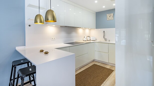 A modern kitchen with white cabinets, a central island, black bar stools, and pendant lighting. - Stunning three bedroom town house walking distance to Puente Romano Hotel (Marbella)