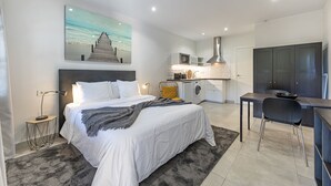 A modern hotel room with a neatly made bed, a dining area, a kitchen, and a large wardrobe. - Stunning three bedroom town house walking distance to Puente Romano Hotel (Marbella)