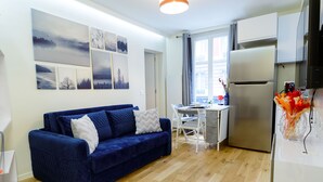 Un espacio habitable compacto con un sofá azul, una mesa de comedor y una zona de cocina que incluye un refrigerador.