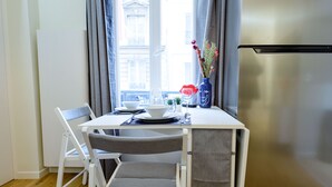 Una cocina compacta con comedor, un refrigerador de acero inoxidable y un ventanal con cortinas.