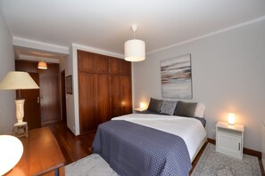 A bedroom with a large bed, wooden wardrobe, bedside lamps, and a marble floor. - Atlantic Dream View - Apartment for 4 with amazing sea views in great location (Nazaré)