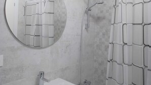 A bathroom with a round mirror, a shower with a white curtain, and a sink with a chrome faucet. - Apartamento Pamplona (Pamplona)