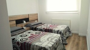A small, clean room with two beds, a nightstand, a lamp, and a window with blinds. - Apartamento Pamplona (Pamplona)