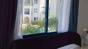 Una habitación con cama, ventana con cortinas y vista a un edificio con balcones.