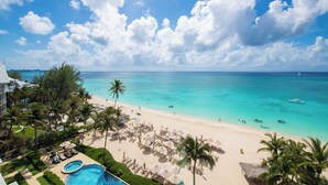 A beach resort with a pool, palm trees, and a view of the ocean. - Beachcomber 41 by Grand Cayman Villas (7 Mile Beach)