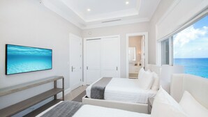A modern bedroom with two beds, a TV, and a view of the ocean. - Beachcomber 41 by Grand Cayman Villas (7 Mile Beach)
