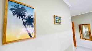 A hallway with a large framed picture of palm trees on the left and a smaller framed picture on the right. - En Micro Centro, Luminoso, Ubicación Ideal (Puerto Iguazú)