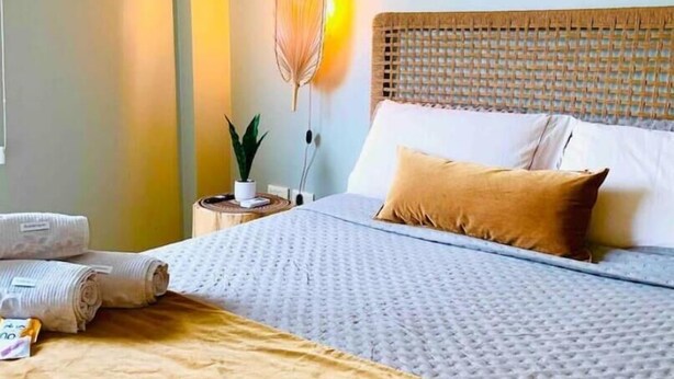 A neatly made bed with a textured white cover, a wooden headboard, and a single brown pillow. - En Micro Centro, Luminoso, Ubicación Ideal (Puerto Iguazú)