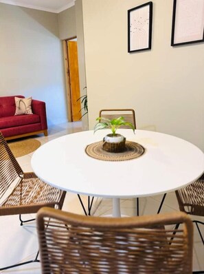 A dining area with a round white table, wicker chairs, a red sofa, and two framed artworks on the wall. - En Micro Centro, Luminoso, Ubicación Ideal (Puerto Iguazú)