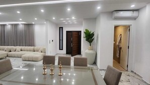 Una sala de estar moderna con una mesa de comedor de vidrio, sofás beige y una planta grande en maceta.