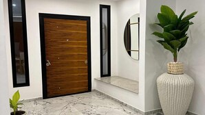 Un pasillo moderno con puerta de madera, espejo, planta en maceta y suelo de mármol.