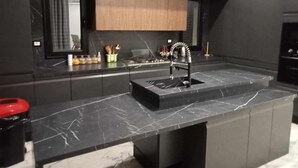 Una cocina moderna con armarios oscuros, encimera de mármol y estufa integrada.